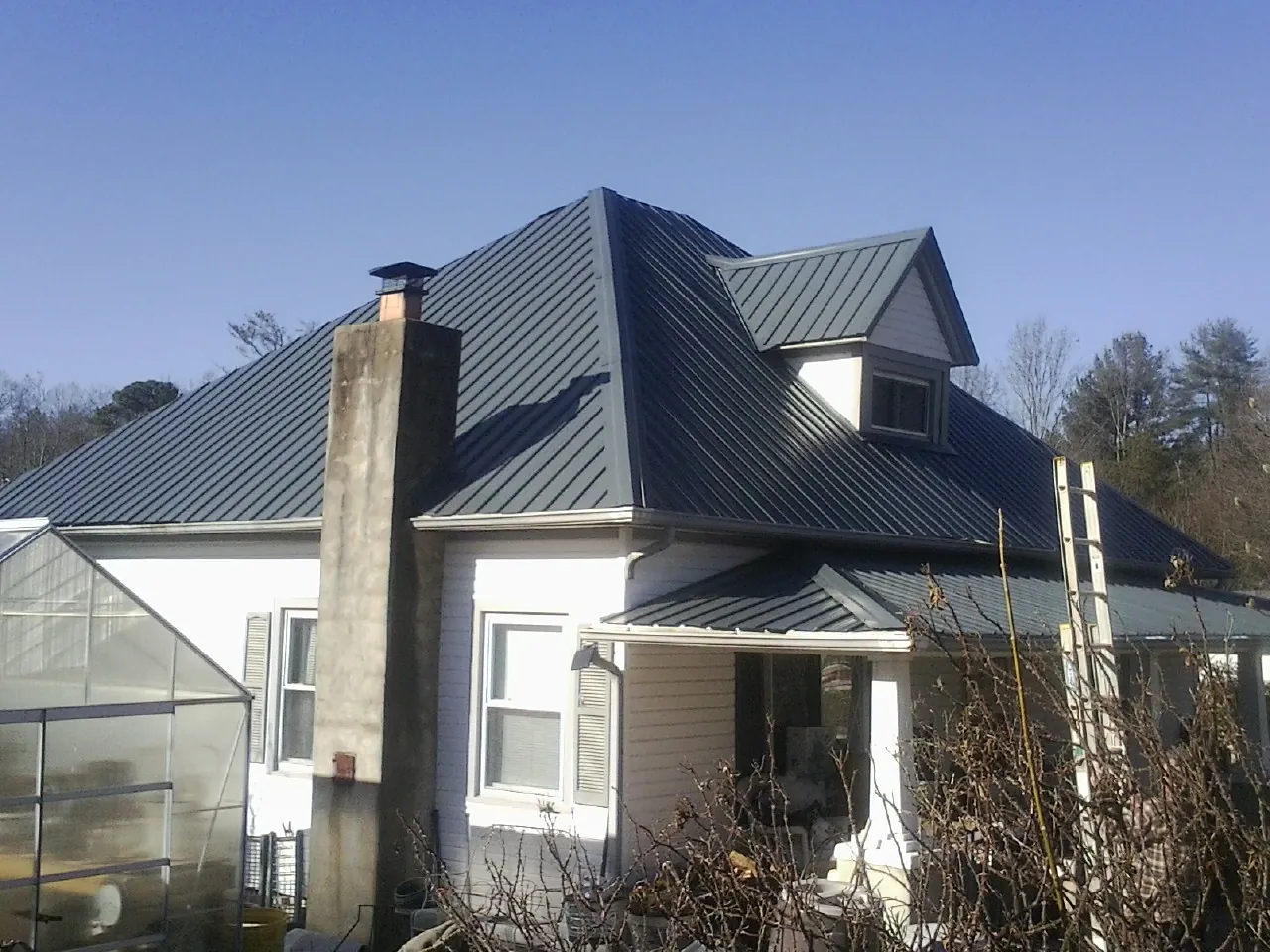 Dark blue standing seam metal roof on a white farmhouse with dormer — Slate & Tile Roof Repair by Roofing Brothers in Holliston