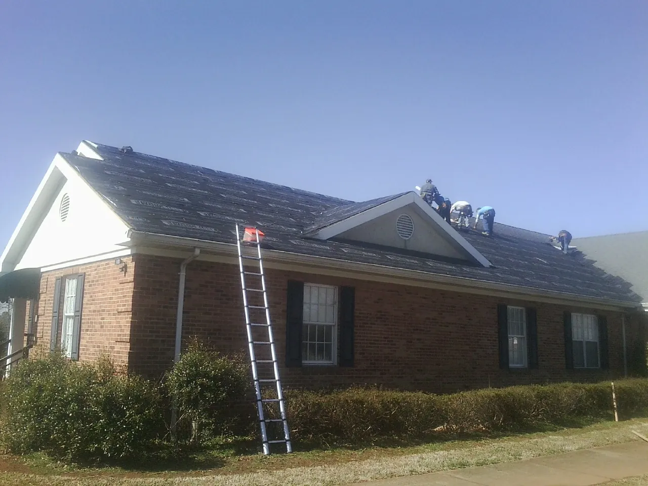 Crew tearing shingles off a brick ranch roof with a ladder set — Metal Roof Repair work by our crew in Holliston