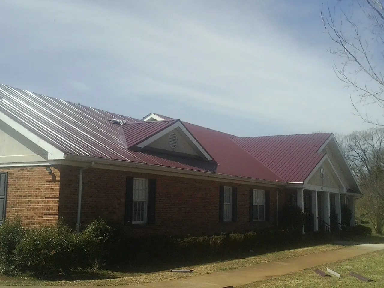 Red metal roof with gabled entries on a long brick building, from a Hail Damage Roof Repair job in Holliston