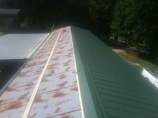 Old rusted panels beside newly installed green metal roofing — Wind Damage Roof Repair by Roofing Brothers in Holliston