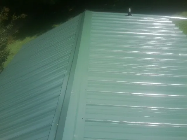 New green metal panels meeting at the ridge of a roof — Flat Roof Repair work by our crew in Holliston