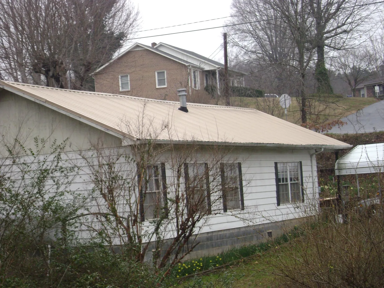 Tan metal roof on a white sided house set into a hillside — Commercial Roofing by Roofing Brothers in Holliston