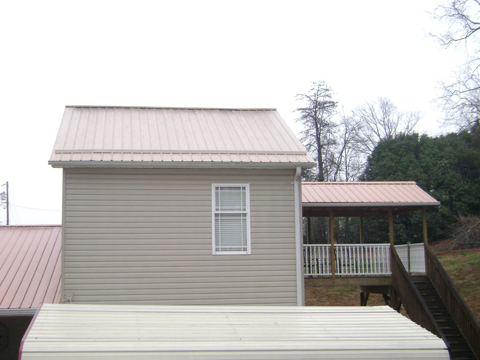 Tan metal roofs on a two story addition and attached porch, from a Roof Replacement job in Holliston