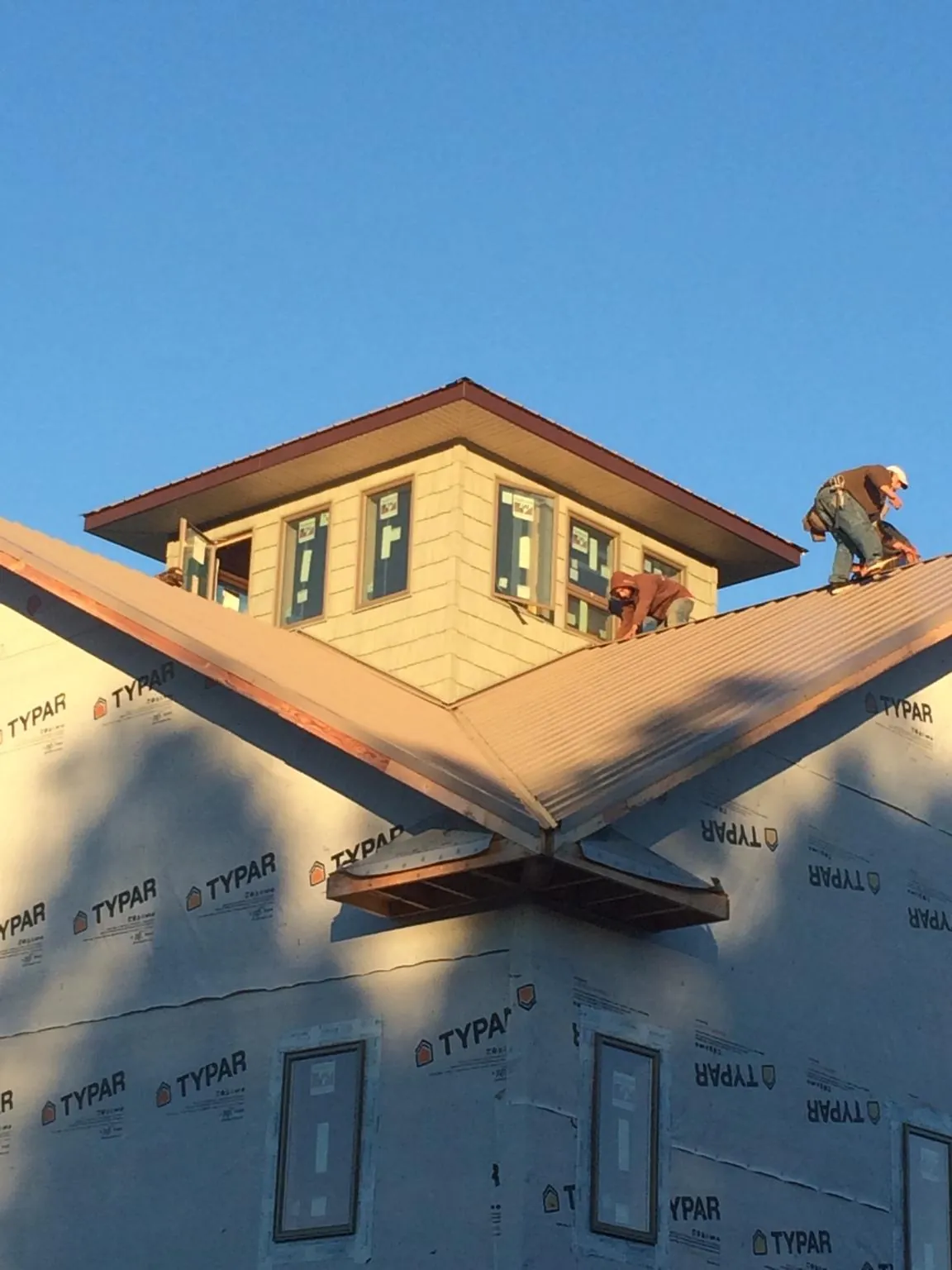 Roofers working around a rooftop cupola on a new metal roof at sunset — Roof Waterproofing in Holliston by Roofing Brothers